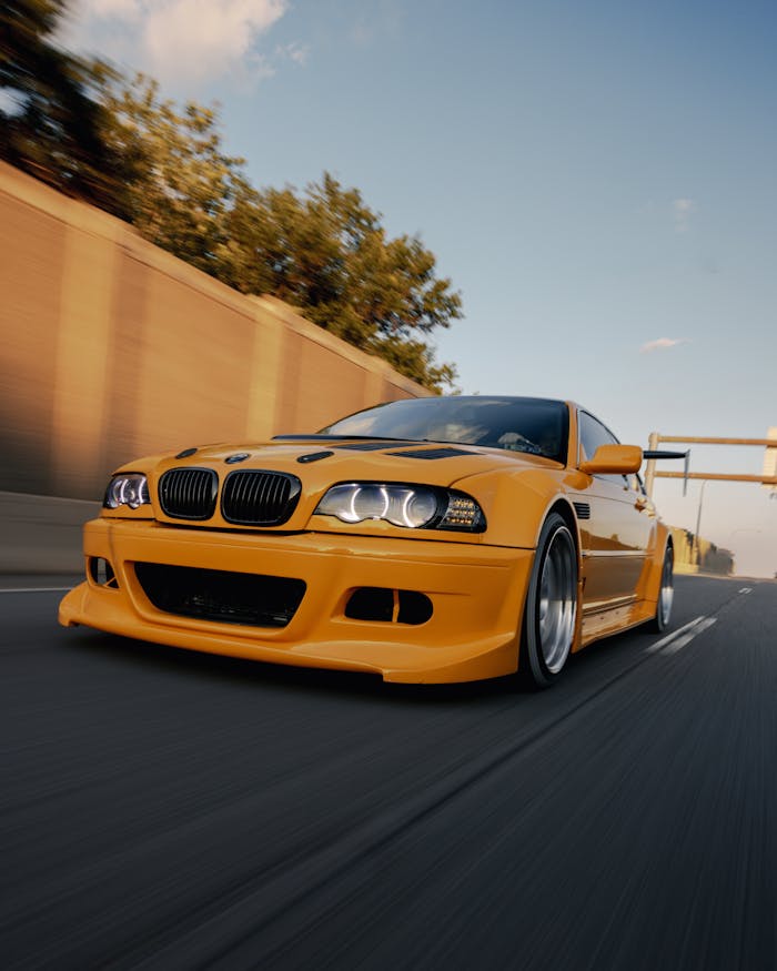 A vibrant yellow BMW E46 racing down a highway in EST